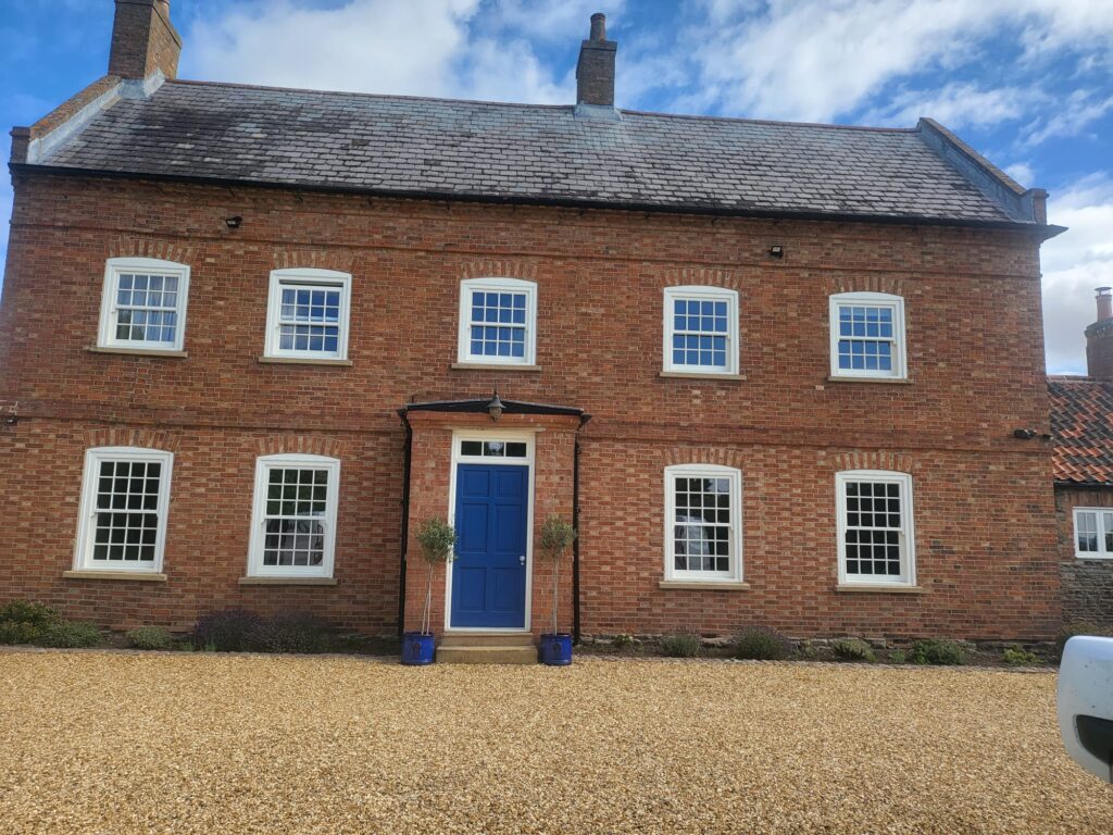 A rustic house with brand new bespoke timber sliding sash windows and a brand new timber royal blue coloured front door.